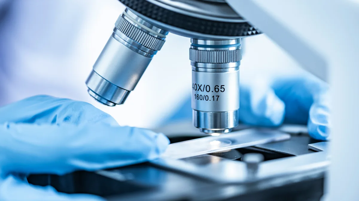 Gloved hand placing a slide under a microscope – Laboratory Services Cooperative data breach class action