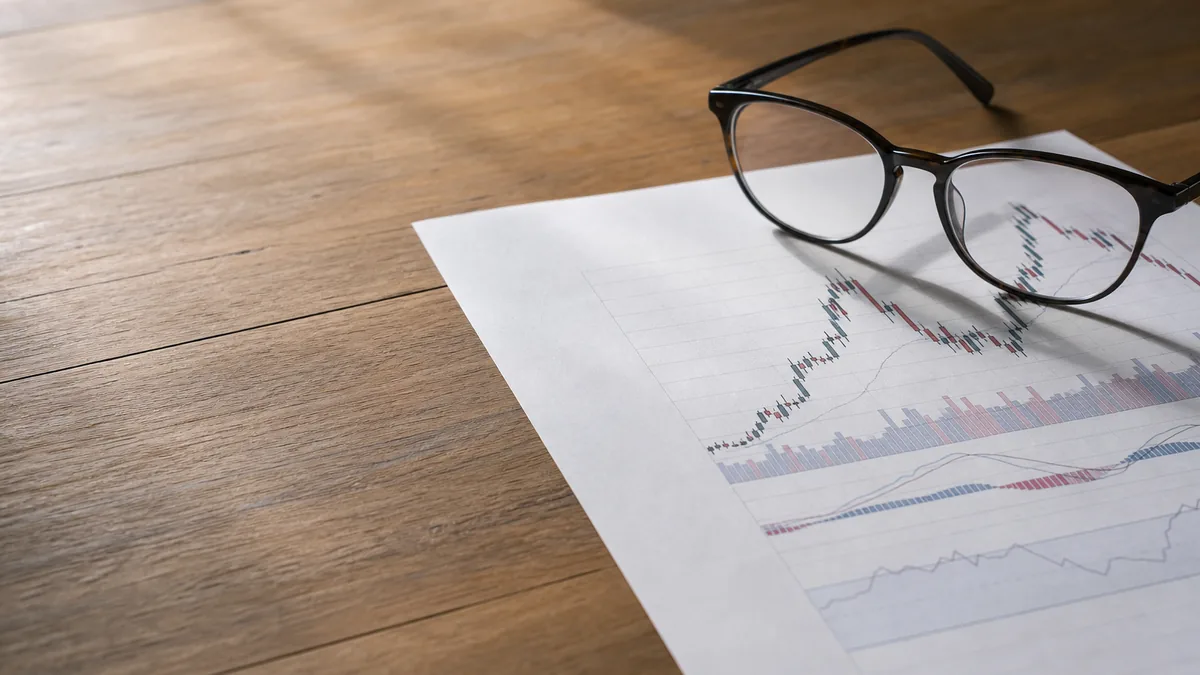 A printed stock chart and reading glasses on a wooden desk, soft daylight